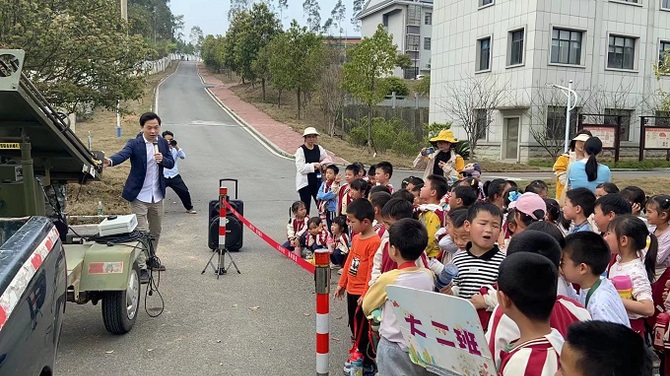 图：江永县气象局工作人员向幼儿园小朋友介绍人工增雨的火箭发射器